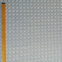 Une règle en bois se tient verticalement le long du bord gauche d'un tissu denim bleu clair 100 % coton avec des œillets floraux brodés, Tissu jean brodé à œillets par Longan Craft France.