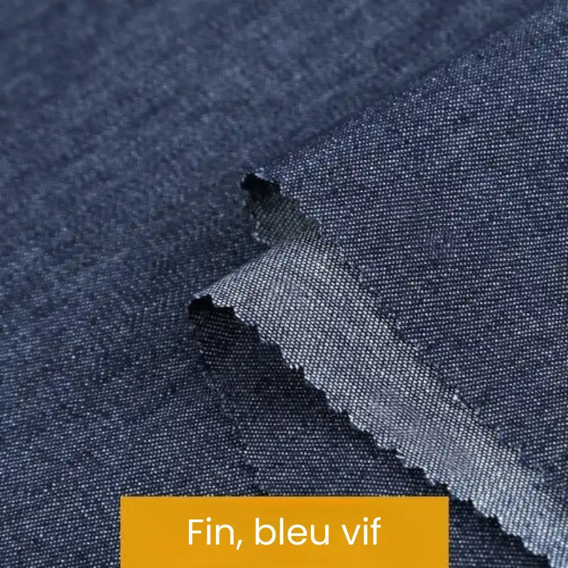 Gros plan sur un tissu denim bleu lisse avec des bords en zigzag. Une étiquette jaune indique "Fin, bleu vif". Issue de la collection Tissu denim coton au mètre de Longan Craft France, cette toile est idéale pour les projets nécessitant des denims de différents grammages.