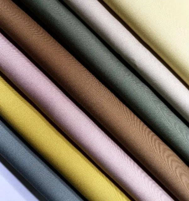 Gros plan sur plusieurs Gabardine de coton au mètre de Longan Craft France, montrant des motifs multicolores en jaune, rose, marron, vert, gris et crème avec un tissage visible sur le tissu gabardine sergée légère pour chemises.