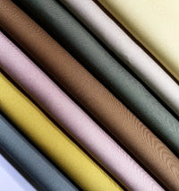 Gros plan sur plusieurs Gabardine de coton au mètre de Longan Craft France, montrant des motifs multicolores en jaune, rose, marron, vert, gris et crème avec un tissage visible sur le tissu gabardine sergée légère pour chemises.
