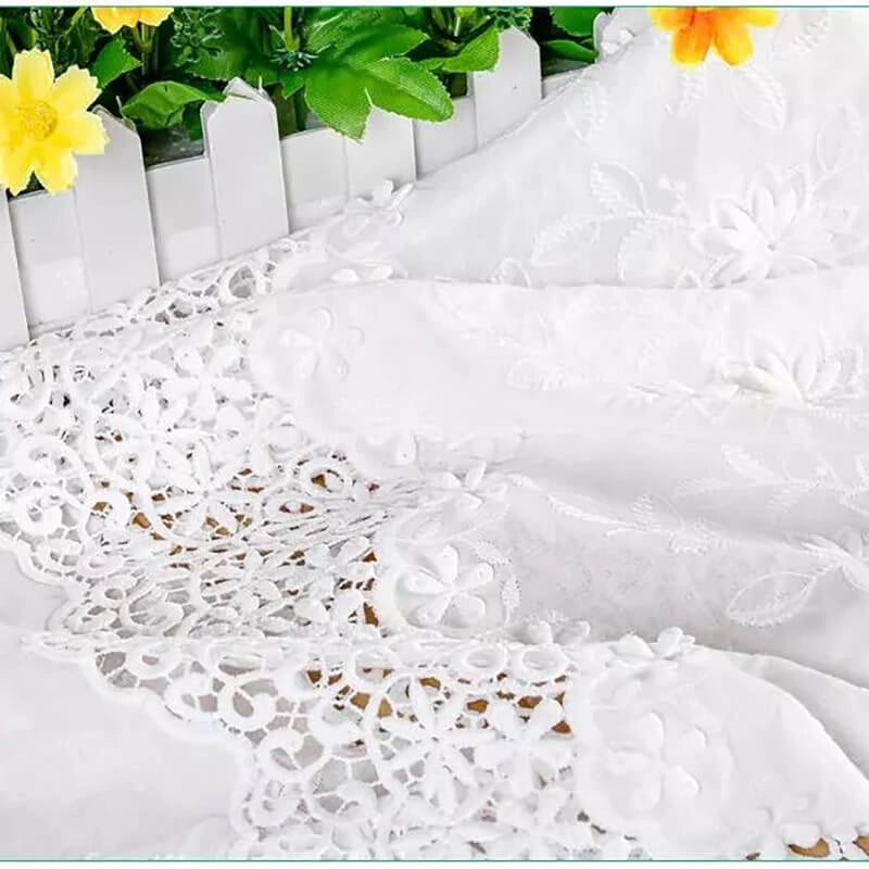 Un gros plan du tissu en coton ajouré 3D brodé œillet au mètre de Longan Craft France est drapé par une clôture blanche, avec des feuilles vertes et des fleurs jaunes en arrière-plan. Parfait pour les vêtements raffinés et les textiles décoratifs.