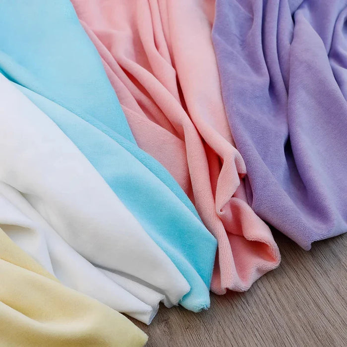 Plusieurs pièces de Longan Craft France Velours de coton et polyester doux au mètre dans les tons pastel jaune, blanc, bleu, rose et violet sont superposées sur une surface en bois. Ce tissu velours doux est idéal pour l'ameublement, l'habillement et les projets de couture.
