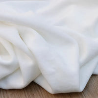 Gros plan sur le Velours de coton et polyester doux au mètre de Longan Craft France, un tissu uni velours doux et lisse aux plis délicats, parfait pour la couture, l'ameublement ou les projets d'habillement. Posé sur une surface en bois.