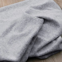 Gros plan sur le Velours de coton et polyester doux au mètre de Longan Craft France en gris clair, avec une texture douce et légèrement chinée, plié librement sur une surface en bois - idéal pour les projets de couture, d'ameublement et d'habillement.