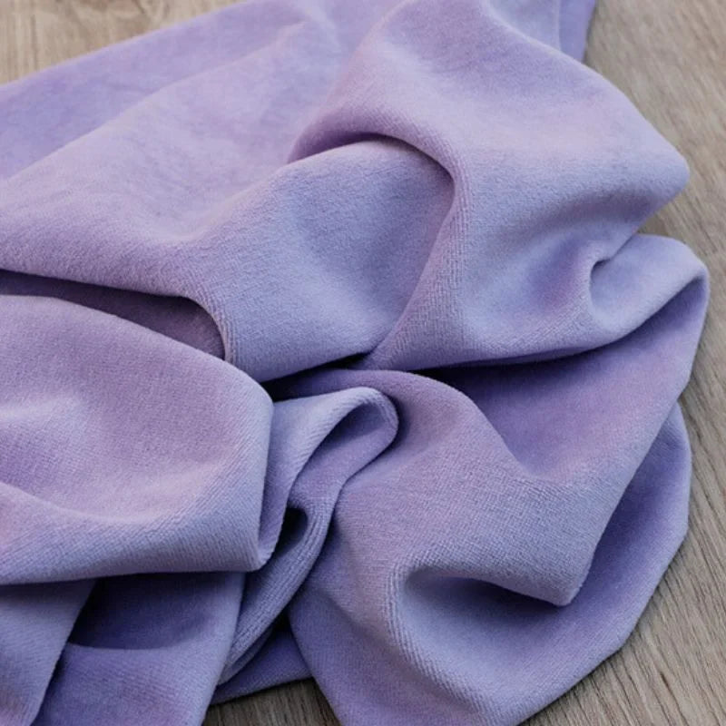 Un morceau de tissu velours coton-polyester de Longan Craft France, vendu au mètre et idéal pour l'ameublement et la couture, est librement drapé et rassemblé sur une surface en bois.