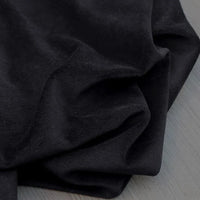 Gros plan sur le Velours de coton et polyester doux de Longan Craft France en noir, montrant sa texture douce et légèrement froissée, drapée sur une surface gris clair - parfait pour l'ameublement, les vêtements et les projets de couture.