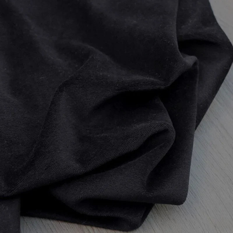 Gros plan sur le Velours de coton et polyester doux de Longan Craft France en noir, montrant sa texture douce et légèrement froissée, drapée sur une surface gris clair - parfait pour l'ameublement, les vêtements et les projets de couture.