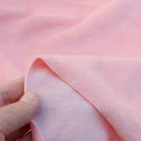 Une main tient le coin de Velours de coton et polyester doux au mètre Longan Craft France, montrant le devant lisse et le dos texturé de ce tissu velours uni idéal pour ameublement, habillement et couture.