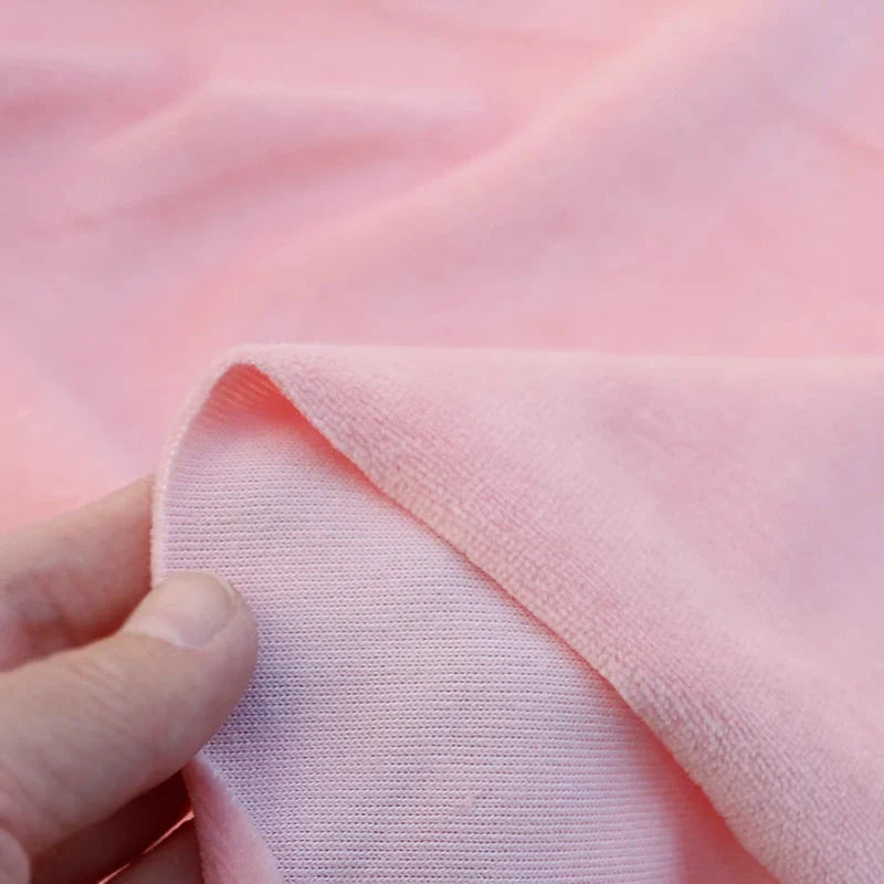 Une main tient le coin de Velours de coton et polyester doux au mètre Longan Craft France, montrant le devant lisse et le dos texturé de ce tissu velours uni idéal pour ameublement, habillement et couture.
