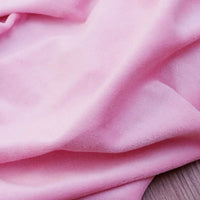 Gros plan sur le Velours de coton et polyester doux au mètre de Longan Craft France, un tissu velours rose pâle uni en maille avec des plis doux et une texture légèrement duveteuse, idéal pour l'ameublement, l'habillement et la couture.