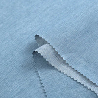 Un gros plan de Tissu denim coton au mètre de Longan Craft France montre la texture lisse et la coupe en zigzag du tissu bleu clair 100 % coton, révélant la trame de ce denim disponible en noir et bleu, différents grammages.