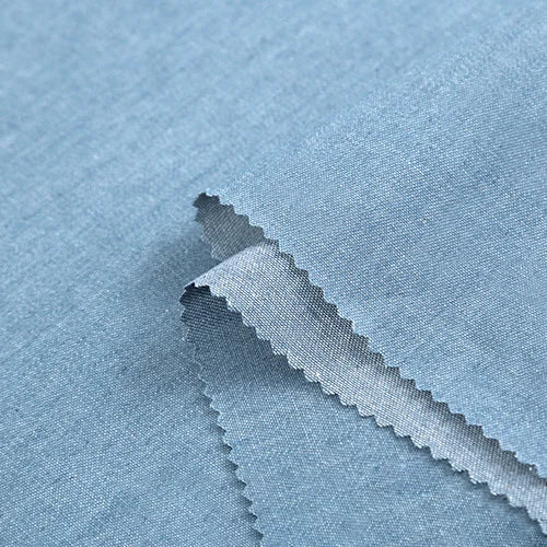 Un gros plan de Tissu denim coton au mètre de Longan Craft France montre la texture lisse et la coupe en zigzag du tissu bleu clair 100 % coton, révélant la trame de ce denim disponible en noir et bleu, différents grammages.