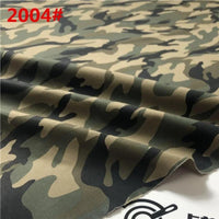 Un gros plan de Tissu sergé camouflage en coton au mètre de Longan Craft France montre un tissu brossé vert, marron, noir et beige avec "2004#" en rouge en haut à gauche, posé à plat et légèrement plié en bas.