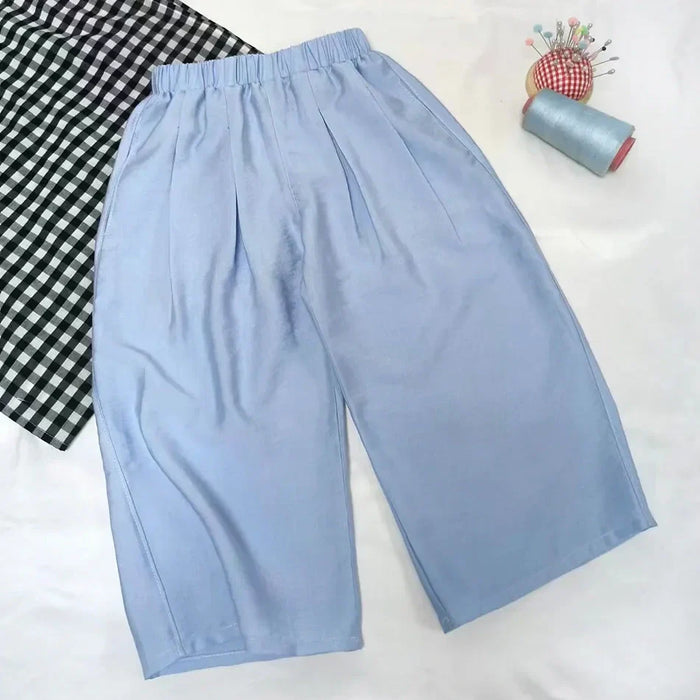 Le Patron de couture pantalon capri à jambes larges de Longan Craft France est présenté sur fond blanc, avec tissu noir et blanc, bobine de fil bleu et coussin à épingles, idéal pour projets débutants. Téléchargement PDF gratuit.