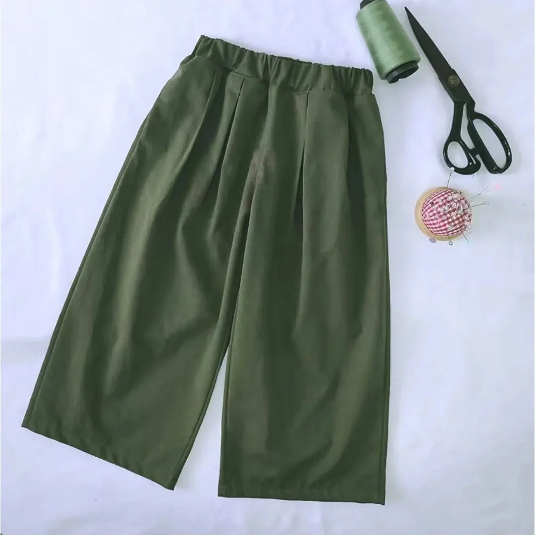 Le Patron de couture pantalon capri à jambes larges de Longan Craft France est présenté sur une surface blanche, accompagné d'une bobine de fil vert, ciseaux noirs et d'une pelote à épingles. Patron PDF gratuit idéal pour débutants couture.