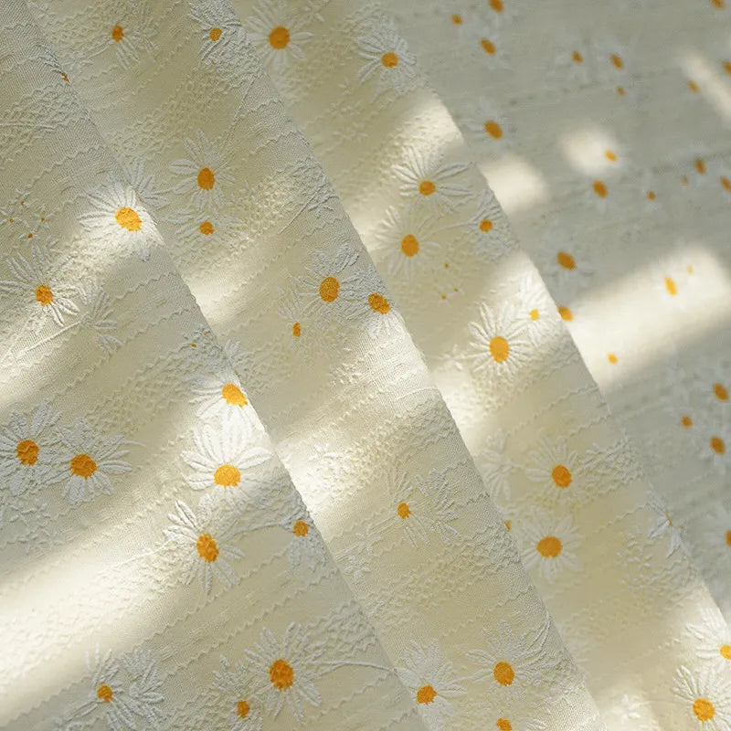 Gros plan sur le Tissu dobby imprimé marguerites au mètre de Longan Craft France, un coton floral crème clair avec des marguerites blanches texturées et des centres jaunes. Idéal pour les vêtements ou la décoration intérieure.