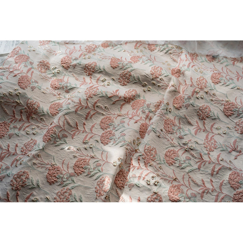 Gros plan sur le tissu brocart pissenlit brodé de Longan Craft France : un jacquard d'ameublement floral vintage avec des broderies texturées roses, vertes et beiges et des accents métalliques dorés. Le tissu est doux et présente une brillance subtile et élégante.