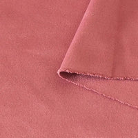 Un gros plan du tissu suédine double face au mètre de Longan Craft France en rose poussiéreux montre sa texture douce en microfibre, son bord plié cousu et son aptitude à être utilisé pour les housses de canapé, les sacs et les doublures.
