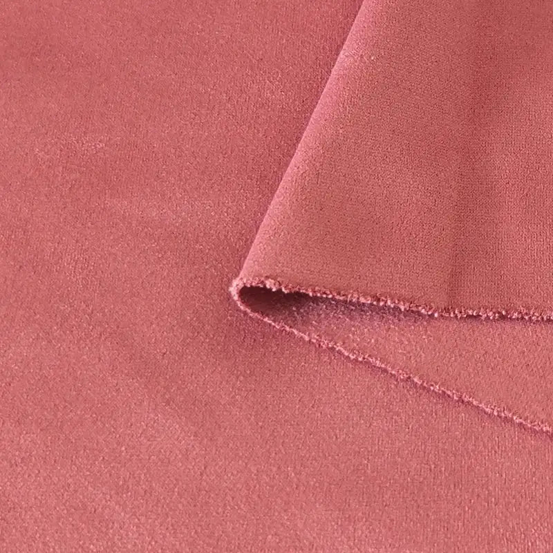 Un gros plan du tissu suédine double face au mètre de Longan Craft France en rose poussiéreux montre sa texture douce en microfibre, son bord plié cousu et son aptitude à être utilisé pour les housses de canapé, les sacs et les doublures.