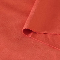 Gros plan sur le tissu suédine corail double face de Longan Craft France, légèrement plié pour révéler sa texture microfibre douce et lisse et son bord non fini, idéal pour les tissus d'ameublement, les sacs ou les doublures.