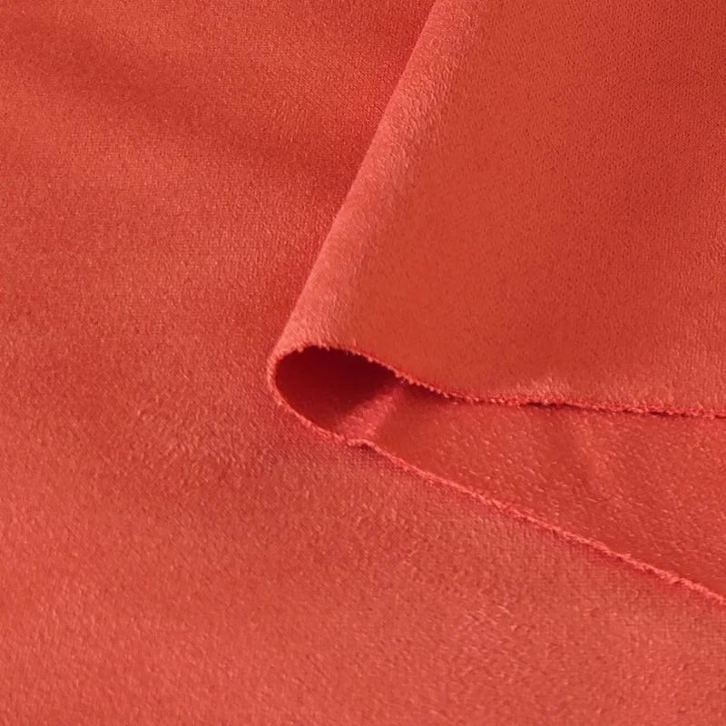 Gros plan sur le tissu suédine corail double face de Longan Craft France, légèrement plié pour révéler sa texture microfibre douce et lisse et son bord non fini, idéal pour les tissus d'ameublement, les sacs ou les doublures.