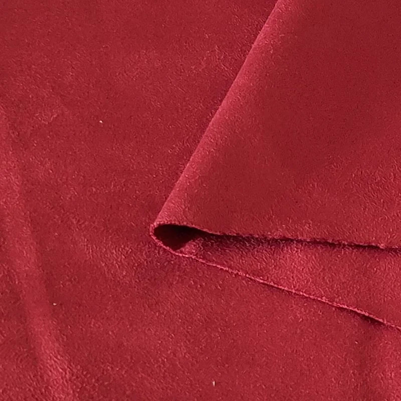 Un gros plan du tissu suédine double face au mètre de Longan Craft France montre sa surface douce et texturée en microfibre. Un coin est plié pour révéler le dessous en imitation cuir suédé, idéal pour les housses de canapé, les sacs et les doublures.
