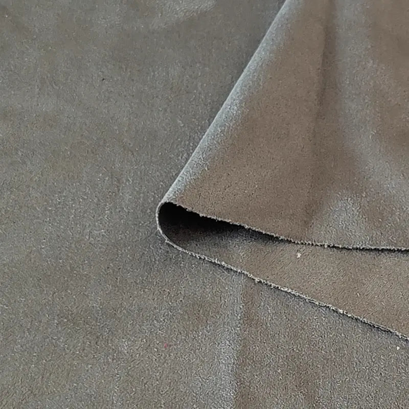 Un gros plan de Longan Craft France Tissu suédine double face au mètre montre un tissu en microfibre gris clair en faux daim, avec un coin plié pour montrer sa texture douce et son épaisseur - idéal pour les housses de canapé, les sacs et les doublures.