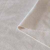 Gros plan sur le Tissu suédine double face au mètre de Longan Craft France, un suédine microfibre beige clair à la texture subtile, aux bords soignés et au léger pliage, idéal pour les housses de canapés, les sacs et les doublures.