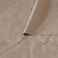 Un gros plan du Tissu suédine double face au mètre de Longan Craft France montre un suédine microfibre beige avec un coin plié, révélant à la fois le recto et le verso - parfait pour les tissus d'ameublement, les sacs et les doublures.