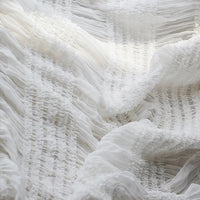 Gros plan sur le tissu mousseline plissé extensible au mètre de Longan Craft France en blanc, révélant une texture froncée et froncée et un aspect doux et transparent, idéal pour les robes plissées et aérées. Disponible en blanc, abricot, rose et noir.
