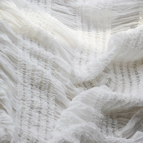 Gros plan sur le tissu mousseline plissé extensible au mètre de Longan Craft France en blanc, révélant une texture froncée et froncée et un aspect doux et transparent, idéal pour les robes plissées et aérées. Disponible en blanc, abricot, rose et noir.