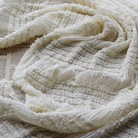 Gros plan sur le tissu mousseline plissé extensible blanc de Longan Craft France, doux et diaphane avec une texture plissée, drapé sur un journal. Idéal pour les robes, ce tissu léger est vendu au mètre en blanc, abricot, rose ou noir.