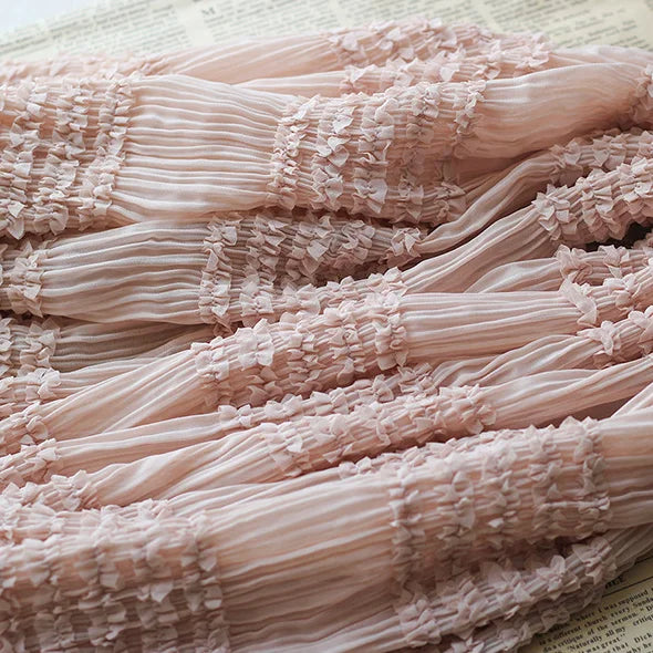 Gros plan sur le tissu rose mousseline plissé extensible au mètre de Longan Craft France, avec des sections froncées et volantées, présenté sur une page imprimée.