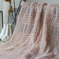 Un tissu mousseline plissé rose pâle de Longan Craft France est drapé sur une surface, avec un vase géométrique blanc et des feuilles séchées en arrière-plan. Disponible au mètre en blanc, abricot, rose et noir pour les robes plissées.