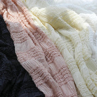 Gros plan sur le tissu mousseline plissé extensible au mètre de Longan Craft France en noir, rose, abricot et blanc, qui présente des plis parallèles et des plis texturés, idéal pour les robes à plis unis.
