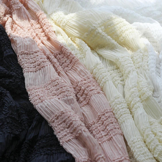 Gros plan sur le tissu mousseline plissé extensible au mètre de Longan Craft France en noir, rose, abricot et blanc, qui présente des plis parallèles et des plis texturés, idéal pour les robes à plis unis.