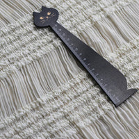 Une règle noire en forme de chat repose sur un tissu mousseline stretch plissé blanc (Longan Craft France), idéal pour les robes plissées, présenté ici dans l'option de couleur uni blanc.