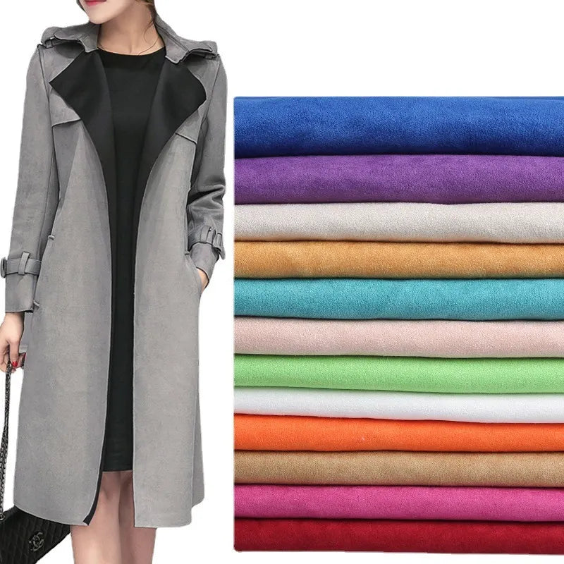 Une personne portant un long manteau gris clair sur une robe noire se tient à côté de Suédine unie embossée au mètre de Longan Craft France, tissu suédé synthétique de haute qualité pour l'habillement, dans les coloris bleu, violet, rose, orange, vert, beige et rouge.