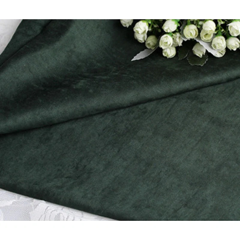 Gros plan sur la Suédine unie embossée au mètre de Longan Craft France, un tissu en daim synthétique de qualité supérieure, présenté sur une surface blanche avec un petit bouquet de fleurs artificielles blanches dans le coin supérieur droit.