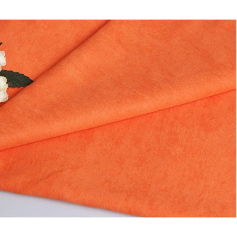 Suédine unie embossée au mètre Longan Craft France, tissu simili cuir synthétique haut de gamme pour vêtements, est soigneusement pliée sur une surface plane avec des fleurs blanches et une feuille verte visible dans le coin supérieur gauche.