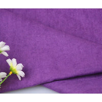 Gros plan sur Suédine unie embossée au mètre de Longan Craft France, un tissu en daim synthétique de haute qualité. Dans le coin inférieur gauche, trois fleurs artificielles blanches avec un centre jaune accentuent la texture douce du simili cuir.
