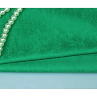 Un gros plan du tissu Suédine Unie Embossée de Longan Craft France - un daim synthétique de première qualité - montre sa texture verte lisse, accentuée par une rangée diagonale de perles blanches dans le coin supérieur gauche.