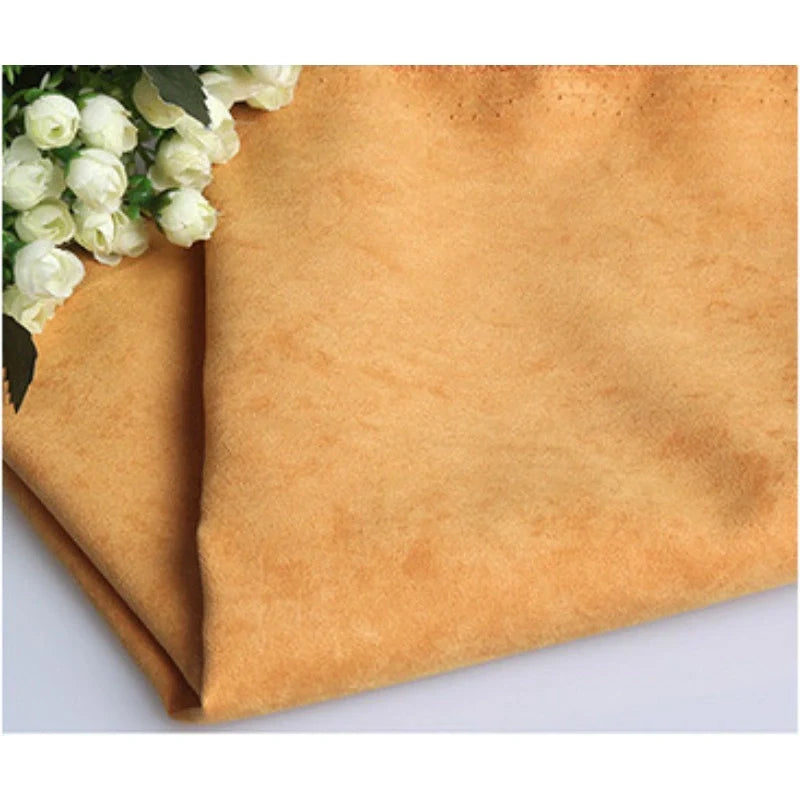 Gros plan sur Longan Craft France Suédine unie embossée au mètre, un tissu en daim synthétique de qualité supérieure pour l'habillement, de couleur marron clair, avec une grappe de roses artificielles blanches dans le coin supérieur gauche.