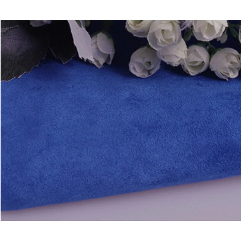 Gros plan sur Suédine unie embossée au mètre de Longan Craft France, un tissu en daim synthétique de qualité supérieure, avec des roses blanches artificielles partiellement visibles dans le coin supérieur droit.