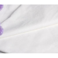 Un gros plan du Suédine unie blanc gaufré au mètre de Longan Craft France montre un léger pli en diagonale, avec quelques fleurs violettes floues dans le coin supérieur gauche. Ce daim synthétique de qualité supérieure est parfait pour l'habillement et l'artisanat.