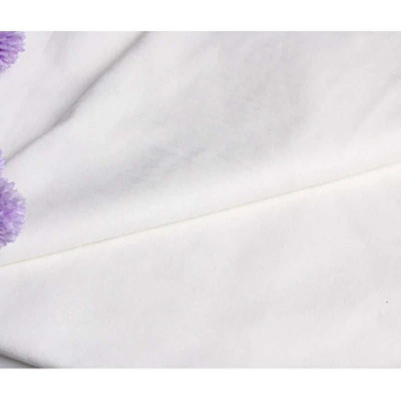 Un gros plan du Suédine unie blanc gaufré au mètre de Longan Craft France montre un léger pli en diagonale, avec quelques fleurs violettes floues dans le coin supérieur gauche. Ce daim synthétique de qualité supérieure est parfait pour l'habillement et l'artisanat.