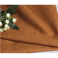 Suédine unie embossée au mètre de Longan Craft France, tissu simili cuir synthétique haut de gamme pour vêtements, drapée sur une surface plane avec un bouquet de fleurs blanches et feuilles vertes à gauche.