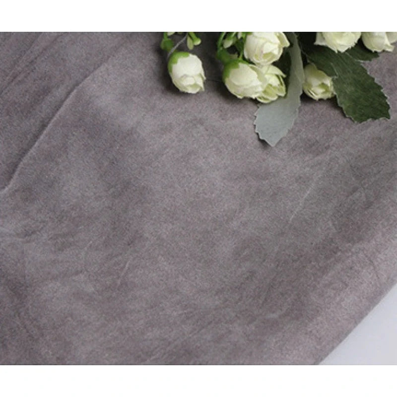 Un bouquet de boutons de rose blancs avec des feuilles vertes repose sur une surface recouverte de Suédine unie embossée au mètre, un tissu en daim synthétique de haute qualité de Longan Craft France. Cette matière douce et légèrement froissée ressemble à du faux cuir de première qualité.