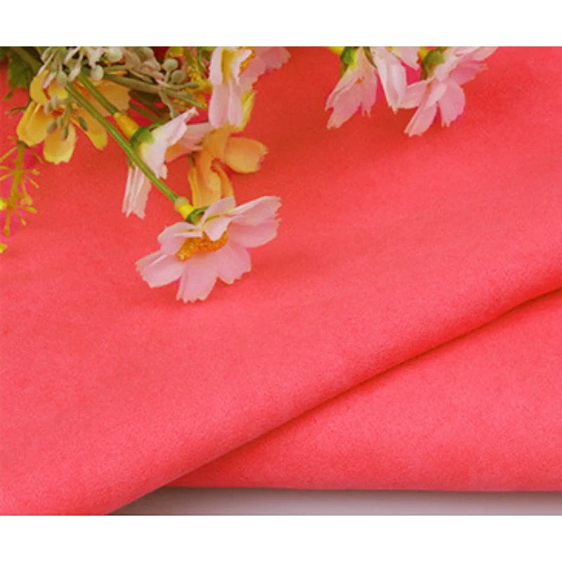 Gros plan sur le pliage de Suédine unie embossée au mètre de Longan Craft France, un tissu en daim synthétique de première qualité, avec des fleurs artificielles roses et jaunes disposées sur le dessus.