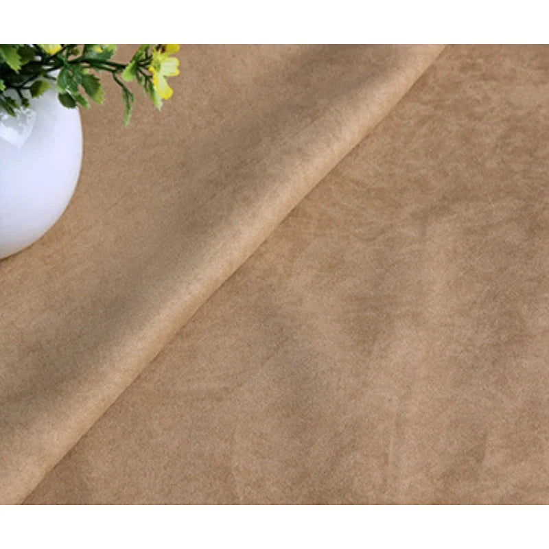 Gros plan sur Suédine unie embossée de Longan Craft France, un tissu en daim synthétique de première qualité, drapé sur une surface plane avec une partie d'un vase blanc avec des fleurs jaunes visibles dans le coin supérieur gauche.
